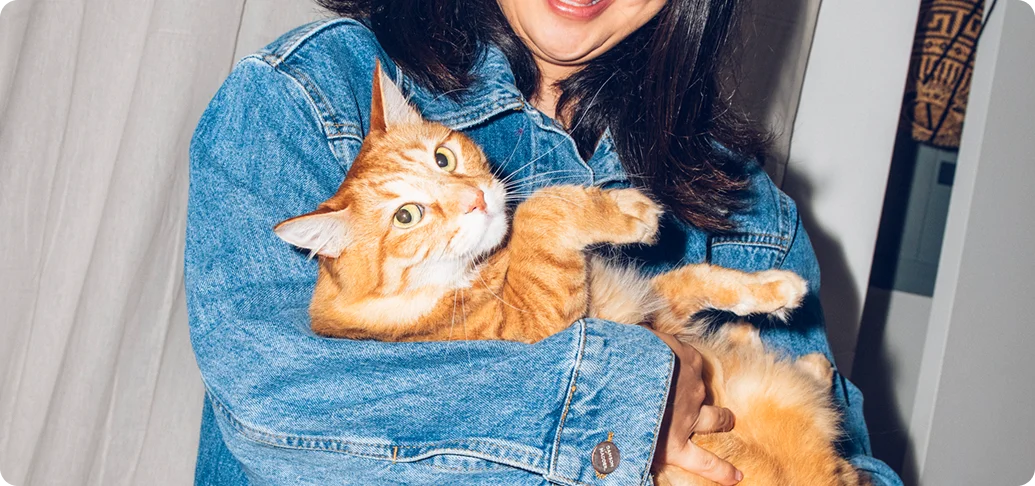 A smiling woman in a denim jacket holding an orange cat