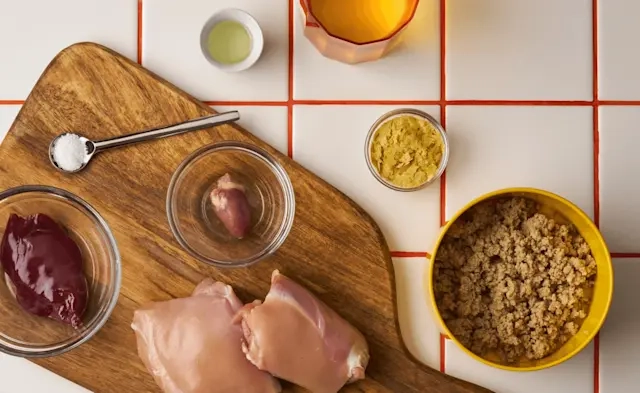 Raw ingredients laid out on a wooden board: meat, vegetables and a bowl of grain